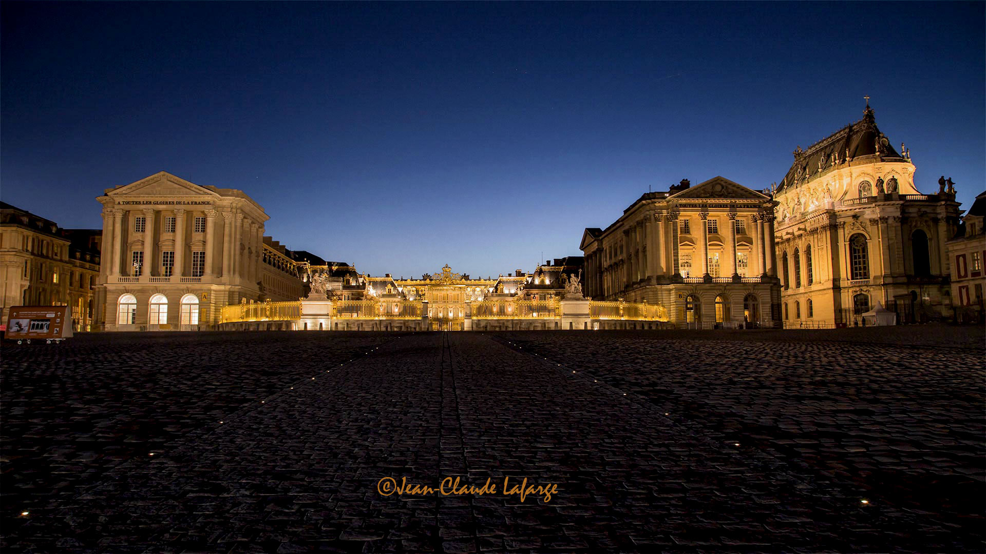 Belle photo de l'entrée du Chateau de Versailles la nuit.